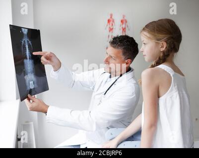 Le docteur en manteau blanc examine le dos de la fille et montre une radiographie Banque D'Images