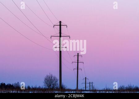 Rangée de lignes électriques près de la route de campagne au coucher du soleil en hiver Banque D'Images