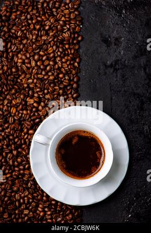 Vue de dessus d'une tasse de café sur fond rustique noir et grain de café. Boisson chaude sur table sombre vintage. Conception artistique minimale. Restaurant c Banque D'Images