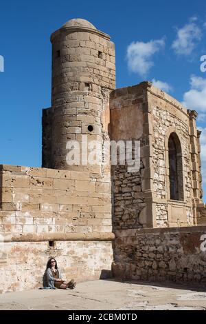 Jeune femme assise contre la forteresse, Essauira, Maroc Banque D'Images