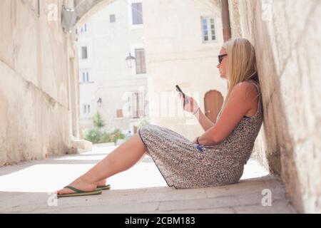 Femme assise sur le sol en utilisant un téléphone portable, Monopoli, Puglia, Italie Banque D'Images