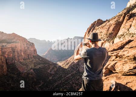 Homme debout sur la montagne, en train de photographier, voir le parc national de Zion, Utah, États-Unis Banque D'Images