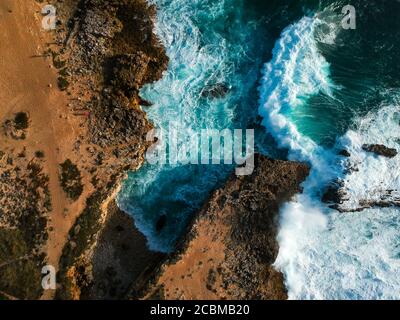 Vue aérienne du dessus des vagues de mer frappant des rochers sur le plage turquoise Banque D'Images