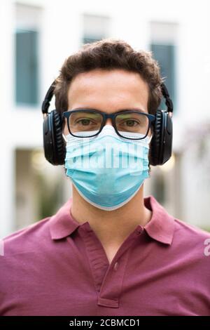 Portrait d'un beau homme dans un masque médial avec des lunettes et des écouteurs. Concept de pandémie de coronavirus. Banque D'Images