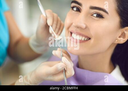 Le dentiste avec des gants à la clinique dentaire examine les dents dans la bouche d'une fille souriante à l'aide d'équipement dentaire. Banque D'Images