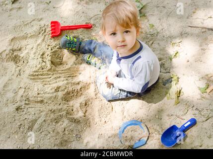 Mignon petit enfant s'amuser avec du sable et des jouets colorés dans le parc, belle journée ensoleillée d'été dans l'aire de jeux pour enfants. Vue de dessus Banque D'Images