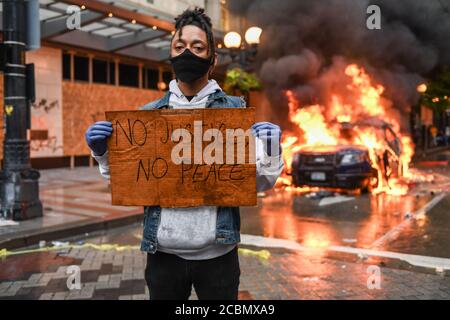 Seattle, USA 30 mai 2020 : tard dans la journée un activiste tenant un panneau NO JUSTICE NO PEACE alors qu'une voiture de police brûle en arrière-plan à Westlake. Banque D'Images