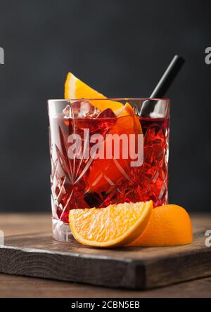 Cocktail Negroni en verre cristal avec tranche d'orange et paille noire sur planche à découper sur fond de bois. Macro Banque D'Images