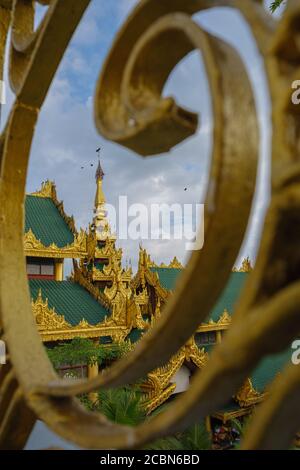 Yangon, Myanmar, Shwedagon Pagode complexe de temple à travers une rampe. Oiseaux volant dans un ciel nuageux. Tir vertical. Pittoresque. Banque D'Images