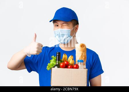 Achat en ligne, livraison de nourriture et concept de pandémie Covid-19. Wencrage gai asiatique courier mâle dans le masque médical, uniforme et gants, assurer bon Banque D'Images