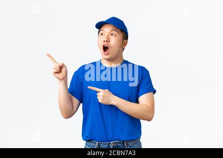 Épatant et impressionné le gars de livraison asiatique en chapeau bleu et un t-shirt à mâchoire goutte surprend et étonne tout en pointant et en regardant coin supérieur gauche Banque D'Images