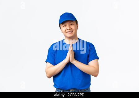 Beau liveur asiatique sympathique, uniforme bleu, tenant les mains dans les plis, paumes ensemble pour remercier, chérissez et valorisez les clients Banque D'Images