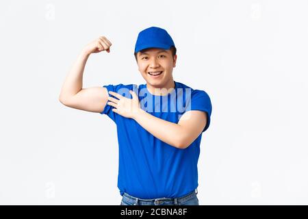 Portrait d'un homme de livraison asiatique souriant et amical montrant ses muscles, des biceps flexibles et regardant heureux, s'assurer que les colis des clients sont en sécurité, porter Banque D'Images