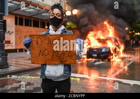 Seattle, USA 30 mai 2020 : tard dans la journée un activiste tenant un panneau NO JUSTICE NO PEACE alors qu'une voiture de police brûle en arrière-plan à Westlake. Banque D'Images