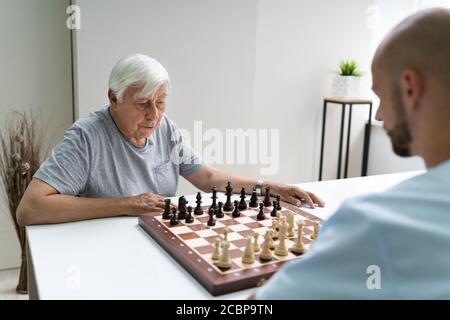 Senior jouant aux échecs avec le soignant à la maison Banque D'Images