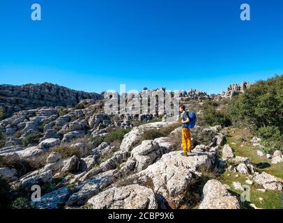 Jeune homme debout sur des rochers et regardant au loin, formations rocheuses calcaires, Réserve naturelle El Torcal, Torcal de Antequera, province de Banque D'Images