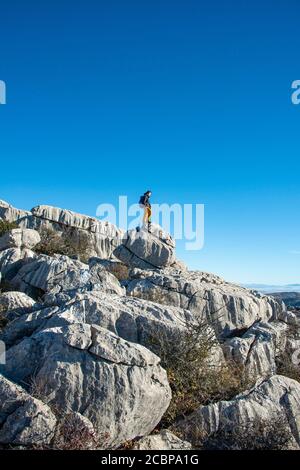 Jeune homme debout sur des rochers et regardant au loin, formations rocheuses calcaires, Réserve naturelle El Torcal, Torcal de Antequera, province de Banque D'Images