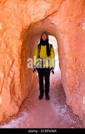 Jeune homme en vêtements d'hiver avec appareil photo, sentier de randonnée à travers le tunnel étroit, randonneur, hiver, Queens Garden Trail, parc national de Bryce Canyon, Utah, États-Unis Banque D'Images