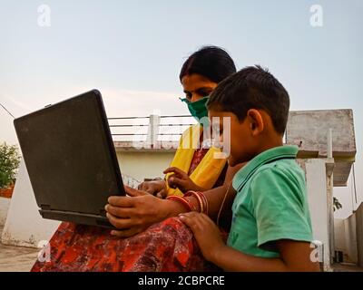 DISTRICT KATNI, INDE - 23 MAI 2020 : une femme indienne pauvre qui apprend la technologie d'un ordinateur portable avec son fils à l'arrière-plan en zone ouverte portant un masque pour corona Banque D'Images