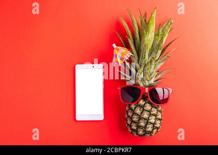 Célébrez le concept de la Journée des ananas d'été, vue du dessus de l'ananas drôle porter des lunettes de soleil rouges et smartphone écran vierge, isolé sur fond rouge, Holid Banque D'Images