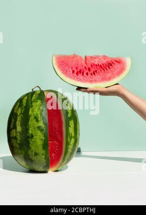 Pastèque fraîche mûre sur fond de couleur menthe néo. Main de femme tenant une tranche de pastèque.Creative minimal fruit d'été concept. Banque D'Images