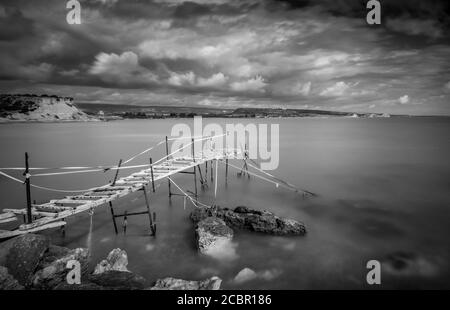 Jetée en bois abandonnée au coucher du soleil. Exposition longue, avec ciel nuageux et orageux. Banque D'Images