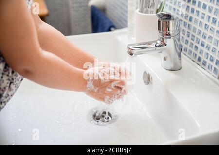 La petite fille se lave les mains avec une barre de savon dans le lavabo sous l'eau du robinet Banque D'Images