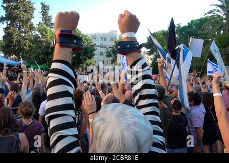 Jérusalem, ISRAËL - 14 AOÛT 2020 : Un manifestant israélien portant un masque avec l'effigie du Premier ministre Benjamin Netanyahu dans un uniforme de prison et des mains manilles participe à une manifestation à laquelle ont assisté plus de 1500 personnes rassemblées à l'extérieur de la résidence officielle du Premier ministre le 14 août 2020 à Jérusalem, en Israël. Les Israéliens sont descendus dans la rue dans des manifestations presque quotidiennes pour appeler à la démission de Netanyahou suite à ses accusations de corruption, accusé de mauvaise gestion de la crise du coronavirus et son agression contre la démocratie. Banque D'Images