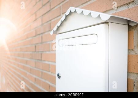 Boîte aux lettres blanche sur le mur de briques d'une maison, avec un arrière-plan non focalisé et une lumière du soleil. Banque D'Images