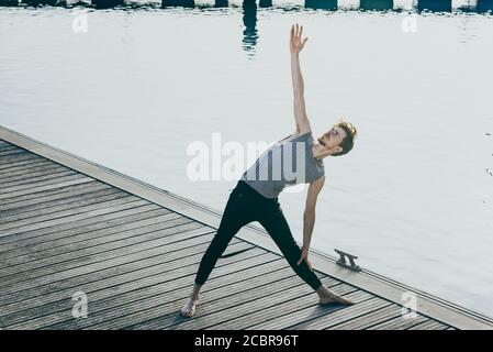 Jeune athlète masculin à poil rouge qui s'étire après l'entraînement pour gagner en flexibilité et détendre ses muscles, à l'extérieur avec un arrière-plan non focalisé. Banque D'Images