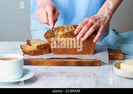 Une femme coupe du pain à la banane sur une planche en bois. Gâteau à la banane Banque D'Images