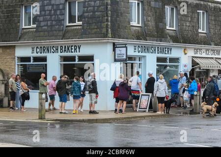 West Bay, Dorset, Royaume-Uni. 15 août 2020. Météo Royaume-Uni. Les vacanciers qui font la queue pour déjeuner devant le Cornish Bakert à la station balnéaire de West Bay à Dorset, lors d'une journée humide et au risque de fortes averses. Crédit photo : Graham Hunt/Alamy Live News Banque D'Images