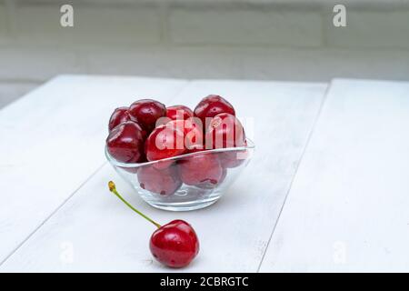 cerises mûres dans un bol en verre sur une table en bois blanc Banque D'Images