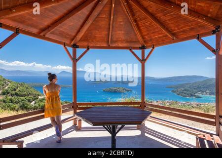 Une femme vêtue de jaune bénéficie d'une vue sur Nidri depuis une rotonde en bois, Lefkada, Iles Ioniennes, Grèce Banque D'Images