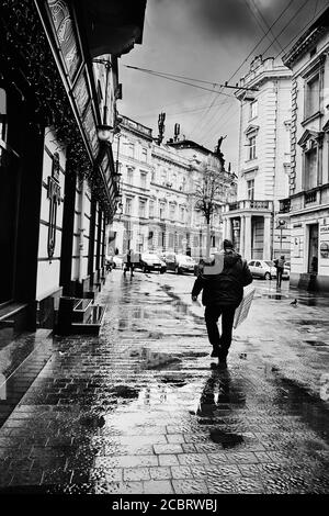 Rue après la pluie. Lviv/Ukraine - 30 janvier 2020 : un liveur porte une boîte vide le long de la rue les Kurbas. Banque D'Images