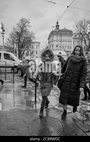 Les filles qui tiennent les mains marchent dans la rue. Lviv/Ukraine - 30 janvier 2020 : les passants marchent sur le trottoir humide de la rue Petra Doroshenka. Banque D'Images