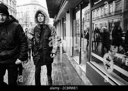 Regardez dans l'appareil photo. Les gars dehors sur un hiver pluvieux jour. Lviv/Ukraine - 30 janvier 2020 : les gens marchent le long de la rue Akademika Hnatyuka Banque D'Images