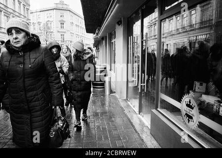 Passants. Lviv/Ukraine - 30 janvier 2020 : les femelles marchent le long de la rue Akademika Hnatyuka lors d'un jour pluvieux d'hiver et sont reflétées dans les vitrines de magasin Banque D'Images