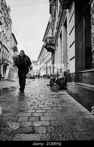 Rue, homme, moto garée. Lviv/Ukraine - 30 janvier 2020 : un homme pensif porte une boîte vide le long de la rue les Kurbas. Banque D'Images