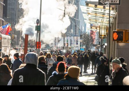 Une foule de personnes s'y promène dans la Midtown Fifth Avenue, sous la vapeur qui s'échappe. Banque D'Images