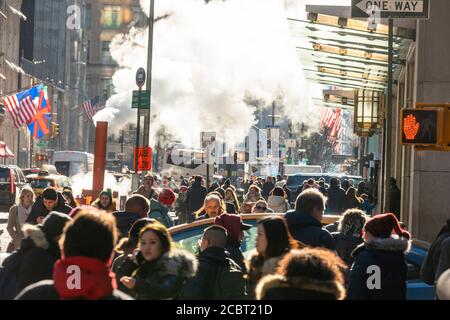 Une foule de personnes s'y promène dans la Midtown Fifth Avenue, sous la vapeur qui s'échappe. Banque D'Images