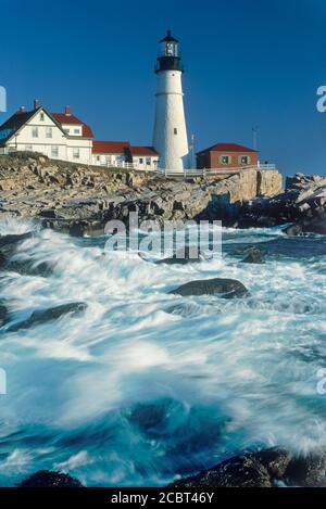 Portland Head Lighthouse dans le Maine au lever du soleil avec des vagues s'écraser sur un rivage rocailleux ci-dessous Banque D'Images