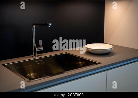 Évier de cuisine noir et eau du robinet dans la cuisine. L'intérieur de la salle de cuisine de l'appartement. Appareils électroménagers. Plaques blanches Banque D'Images
