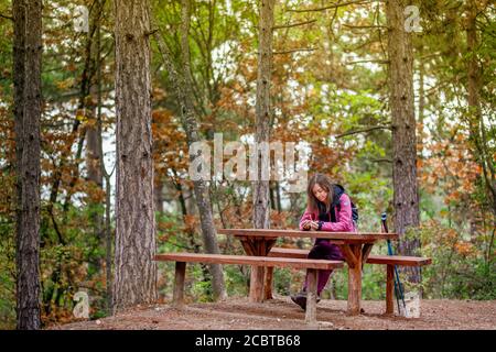 Une jeune fille de randonneurs se reposant sur un banc dans la forêt. Sac à dos avec veste rose dans la nature. Banque D'Images