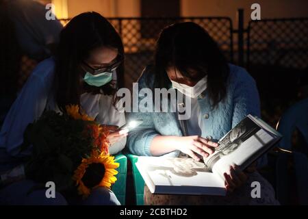 Bucarest, Roumanie. 15 août 2020. Les femmes portant un masque de visage regardent un album d'art avant que le film commence dans un cinéma en plein air à Bucarest, Roumanie, 15 août 2020. Le gouvernement roumain maintient la fermeture des cinémas et des théâtres dans le contexte de la pandémie COVID-19, mais permet des films ou des spectacles en plein air avec un public limité et des réglementations de prévention des épidémies. Credit: Gabriel Petrescu/Xinhua/Alay Live News Banque D'Images