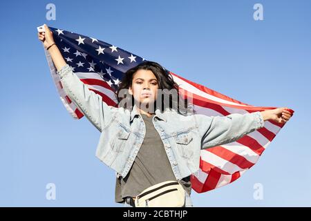 Fière femme afro-américaine debout dans la rue, portant le drapeau des états-unis. Banque D'Images