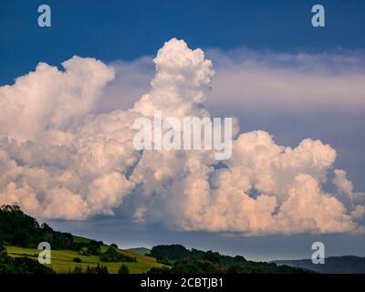 Nuages de pluie massifs - Cumulonimbus - se formant dans le bleu ciel sur paysage vallonné Banque D'Images