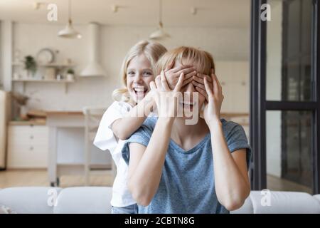 Petite fille naughty fermer les yeux de la mère riant avec des paumes Banque D'Images