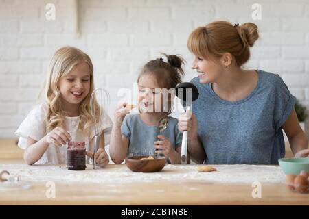 Bonne jeune maman et ses petites filles goûtant des pâtisseries maison Banque D'Images