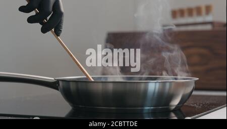 homme main dans des gants en déplaçant quelque chose avec une spatule en bois dans un poêle à frire, photo large Banque D'Images